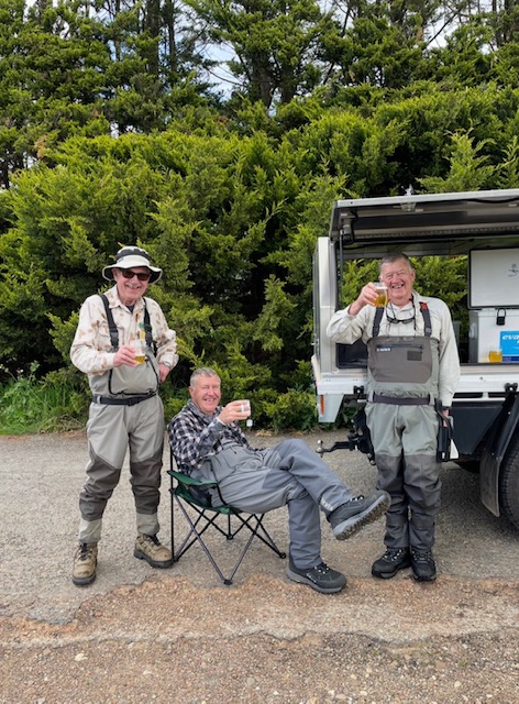 Three anglers in waders sharing a drink beside the vehicle after a session