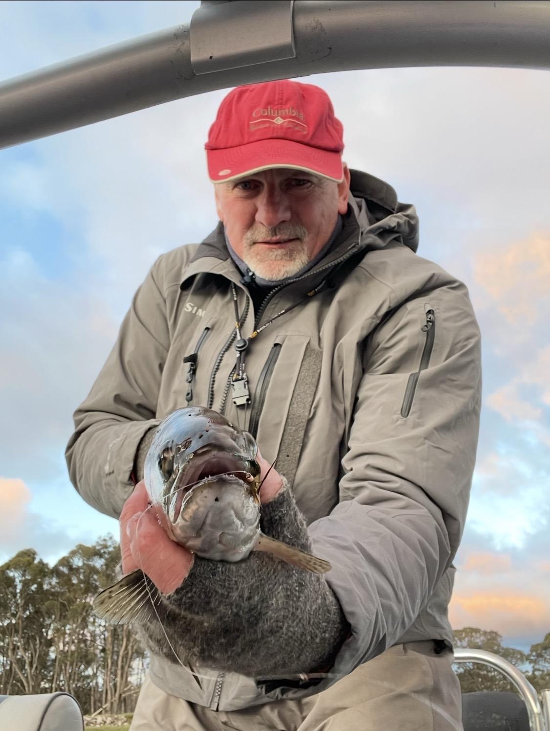Angler in wet-weather gear holding a big lake trout at dusk