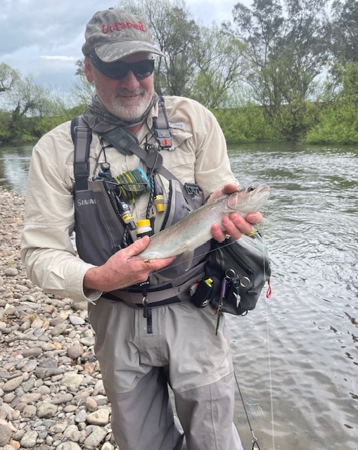 Angler holding a bright rainbow trout on a wide river bank
