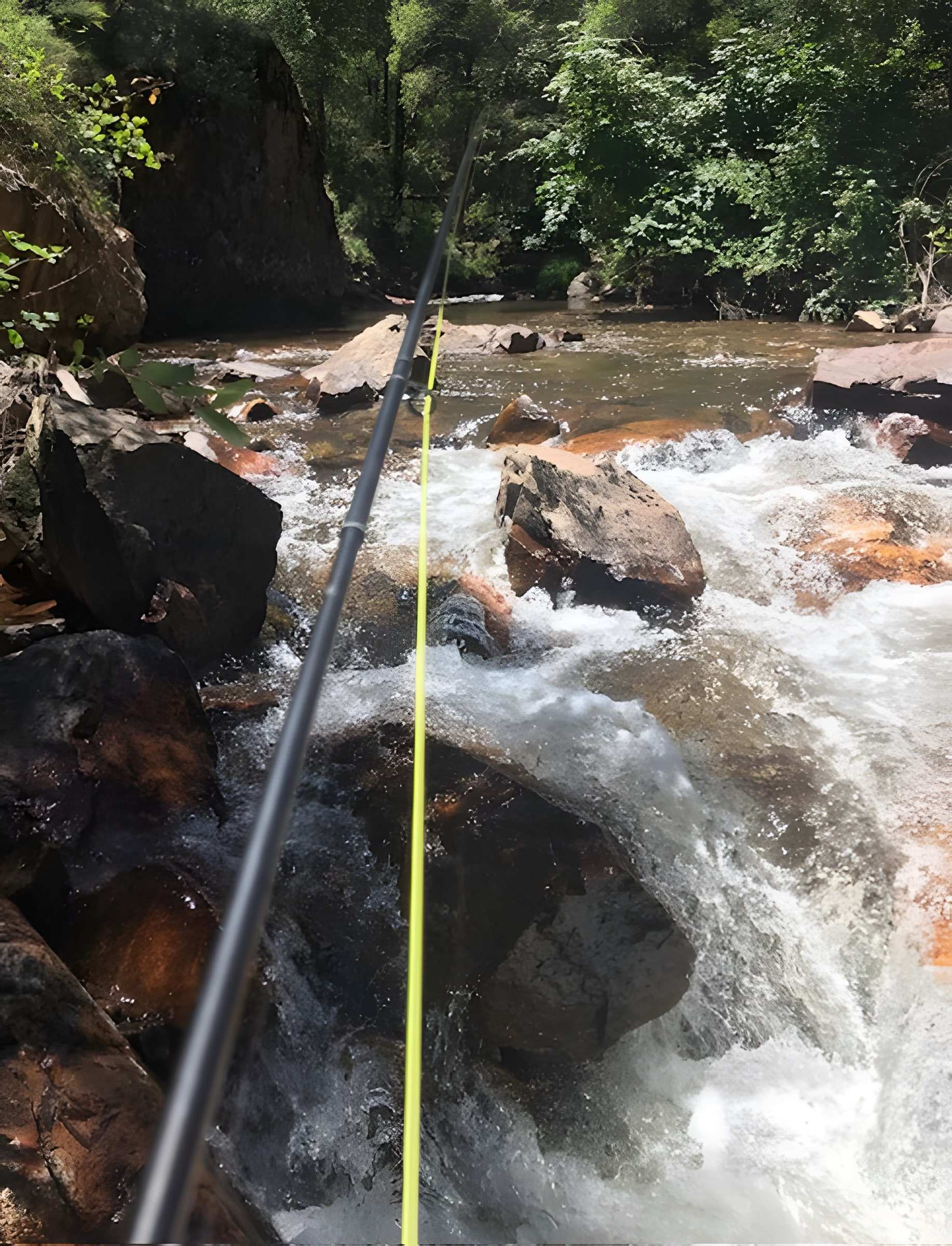 Fly rod held over white water tumbling through boulders